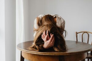 Uma mulher mostrando-se desesperada com seu cabelo sobre a mesa, indicando possível estresse, exaustão e ansiedade.
